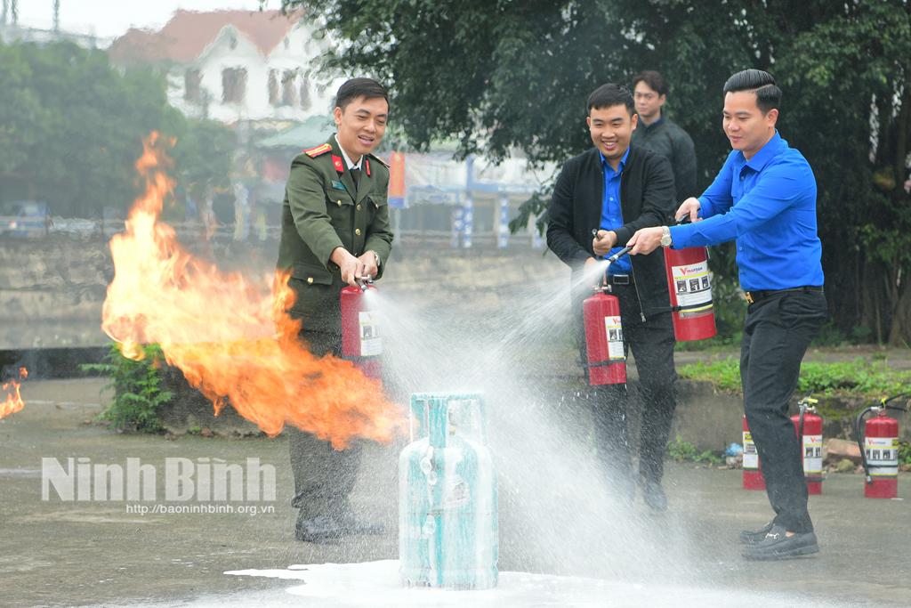 Cán bộ Công an hướng dẫn thanh niên cách sử dụng bình cứu hoả. Ảnh: Trường Giang