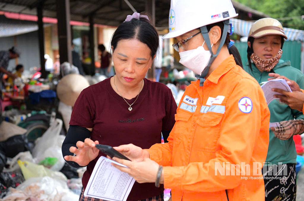 Nhân viên Công ty Điện lực Ninh Bình hướng dẫn người dân xã Vạn Thắng thanh toán tiền điện không dùng tiền mặt. (Ảnh: Trường Giang)